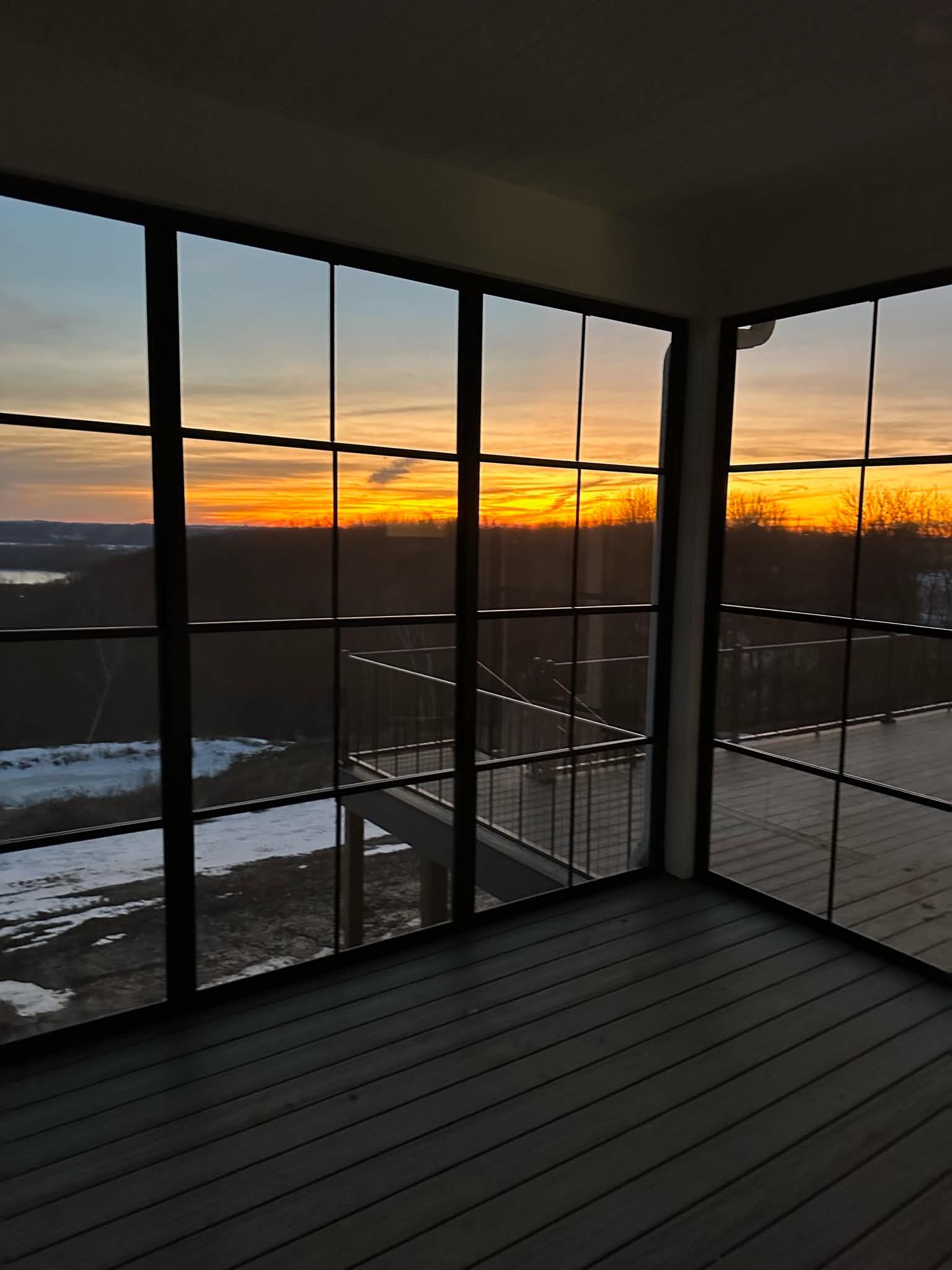 Sunset view from a screened porch with snow-covered ground and dark railing panels