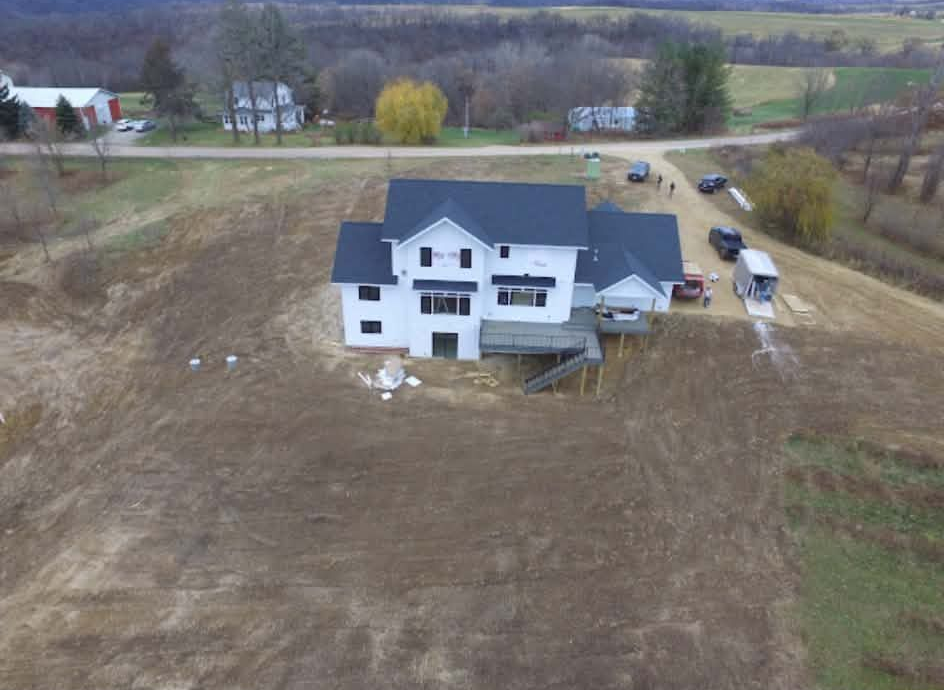 Aerial view of a white two-story house with a dark roof in a rural field