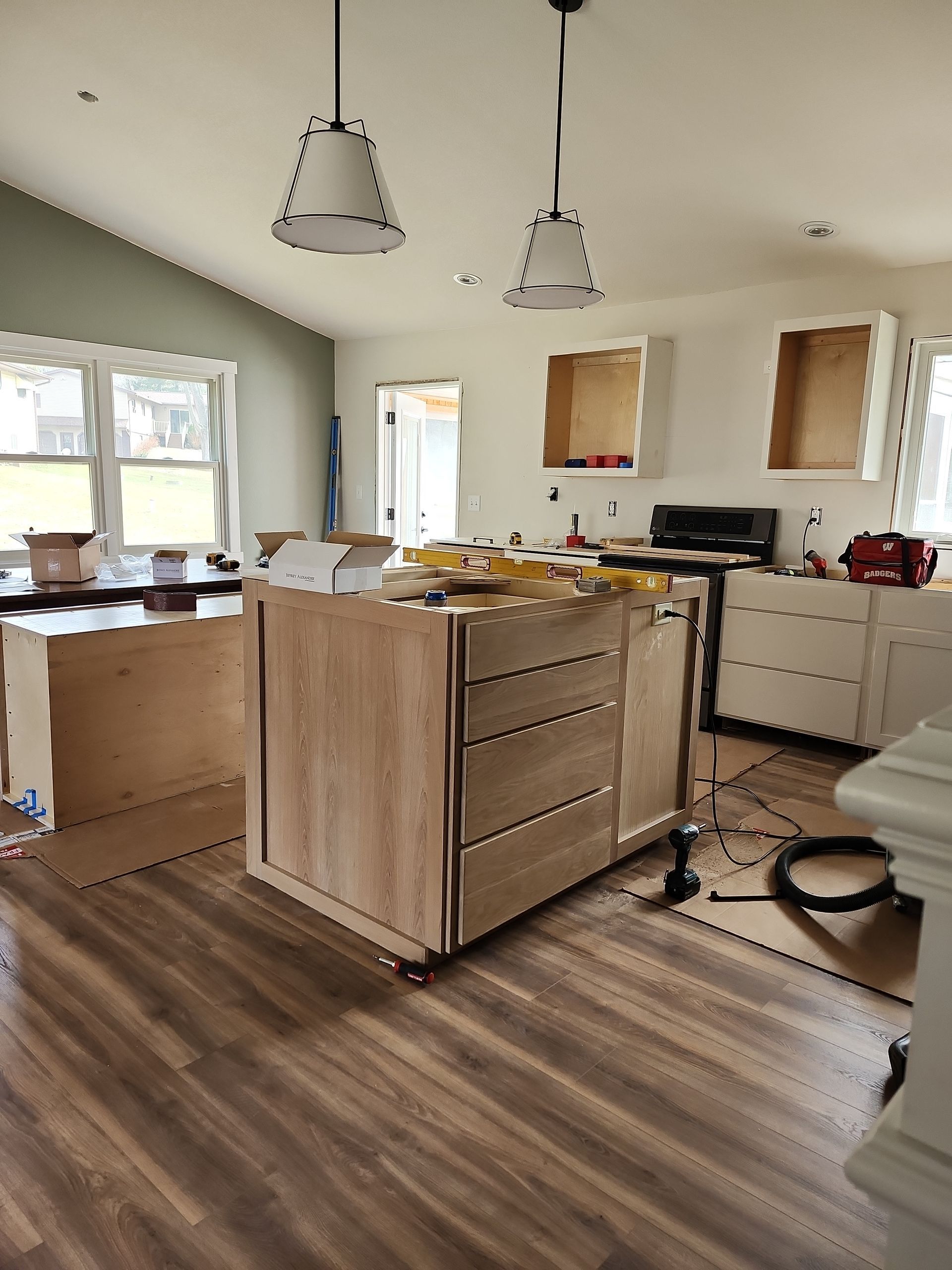 Kitchen under renovation with island, pendant lights, unfinished cabinets, and tools on the floor