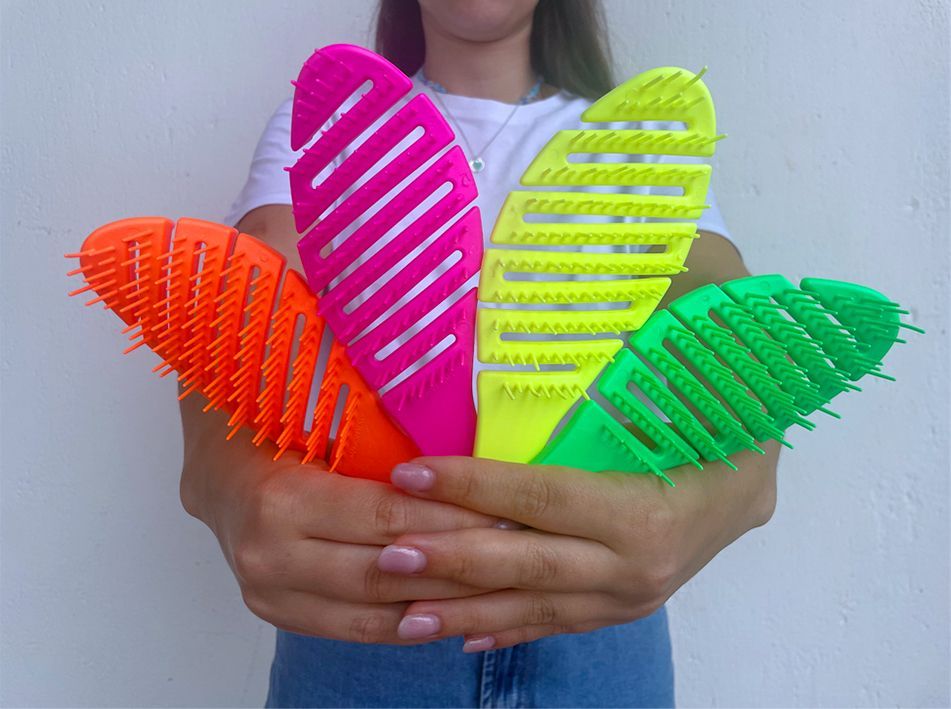 Donna che tiene in mano quattro spazzole per capelli dai colori vivaci e testurizzati, nei colori rosa, arancione, verde e giallo.