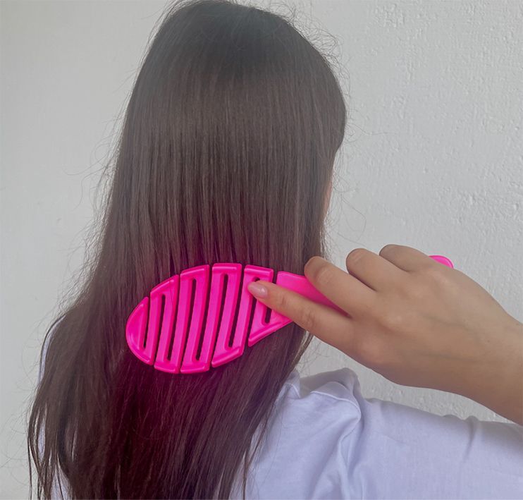 Persona che spazzola i capelli lunghi e scuri con una spazzola rosa contro un muro bianco.