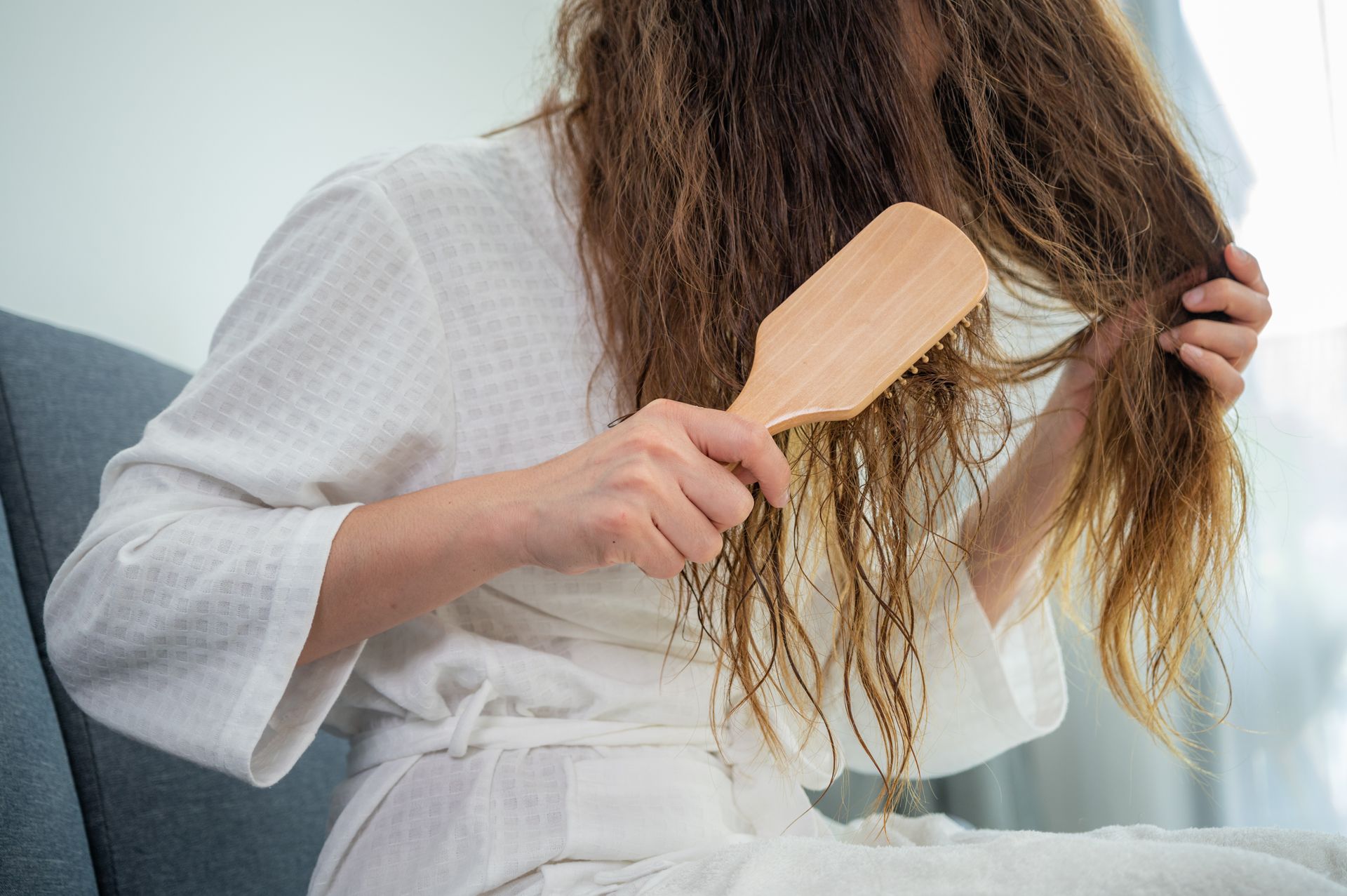 Una donna in tunica bianca si spazzola i capelli con una spazzola di legno.