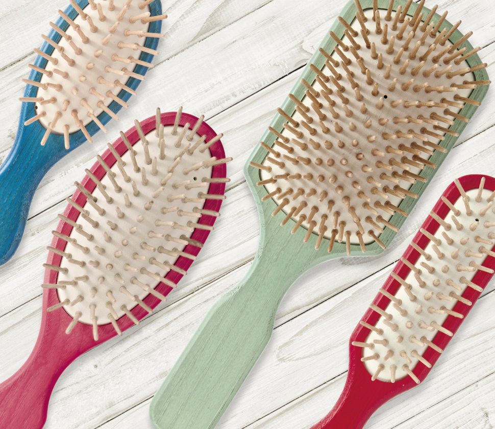Quattro spazzole per capelli di colore diverso sono appoggiate su un tavolo di legno