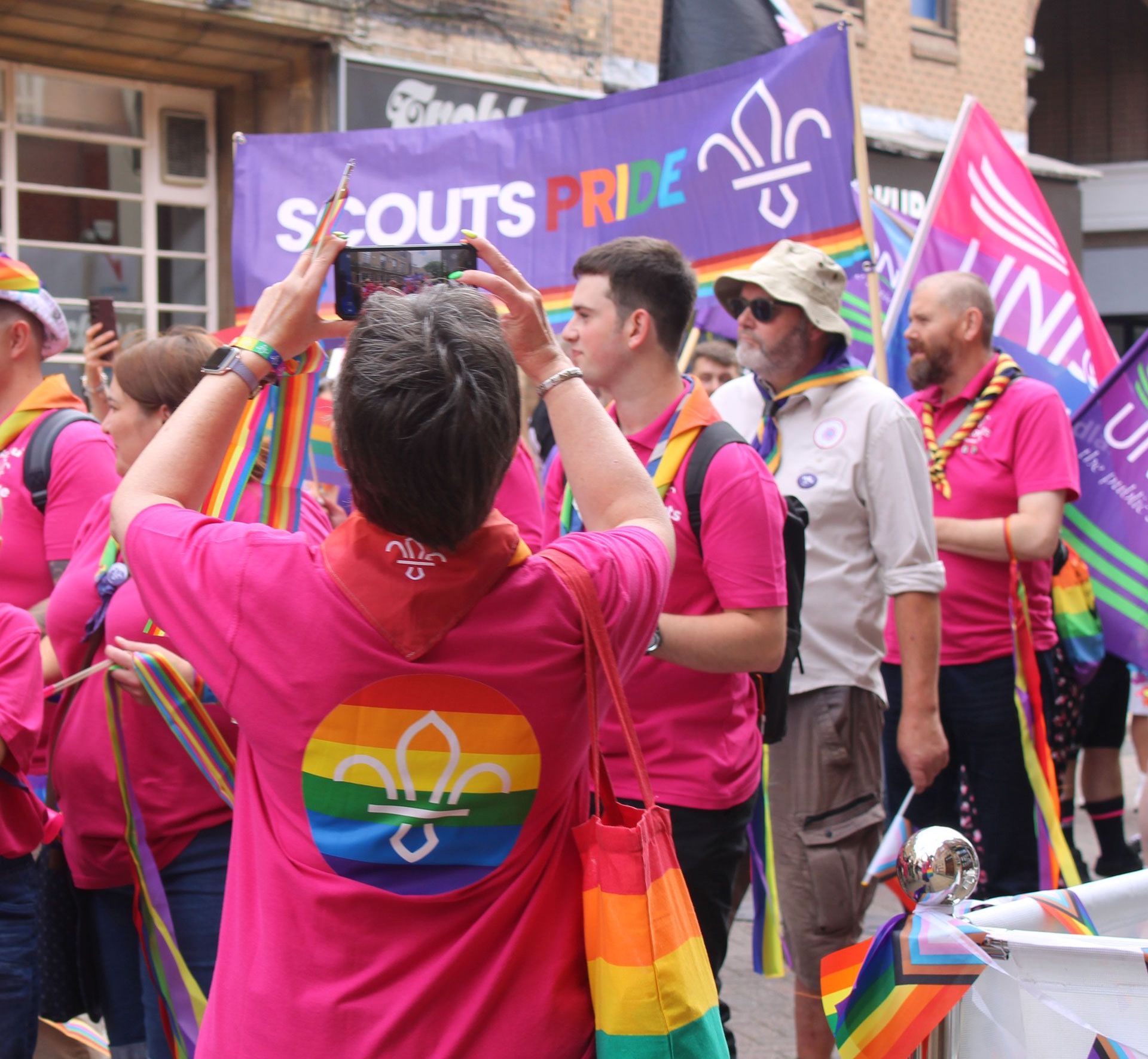 Lincoln Scouts showing their Pride at the 2023 Lincoln Pride parade. Lincoln Scouts members at Pride wearing pink shirts with rainbow Scout logos, standing in front of a Scouts Pride banner and rainbow flags.