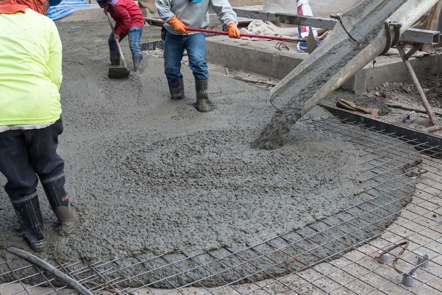 Workers pouring wet concrete onto a paved surface at a construction site