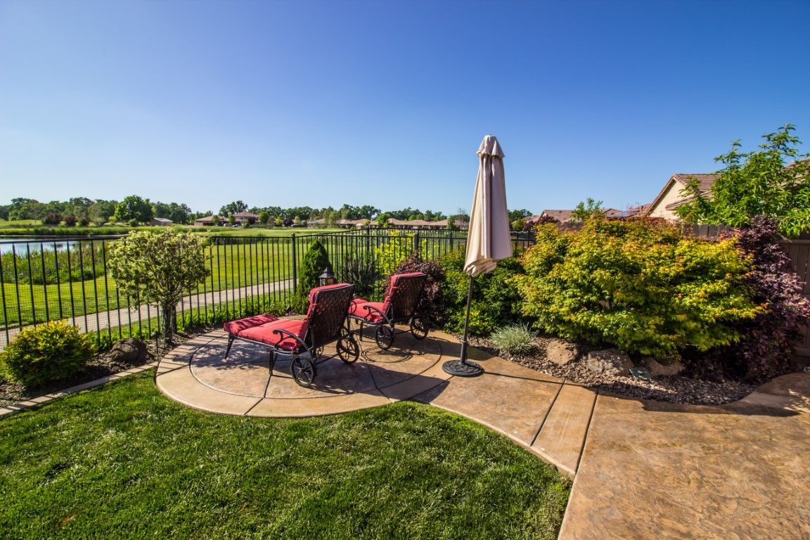 Patio with red chairs, umbrella, and lush garden overlooking a pond under a clear blue sky