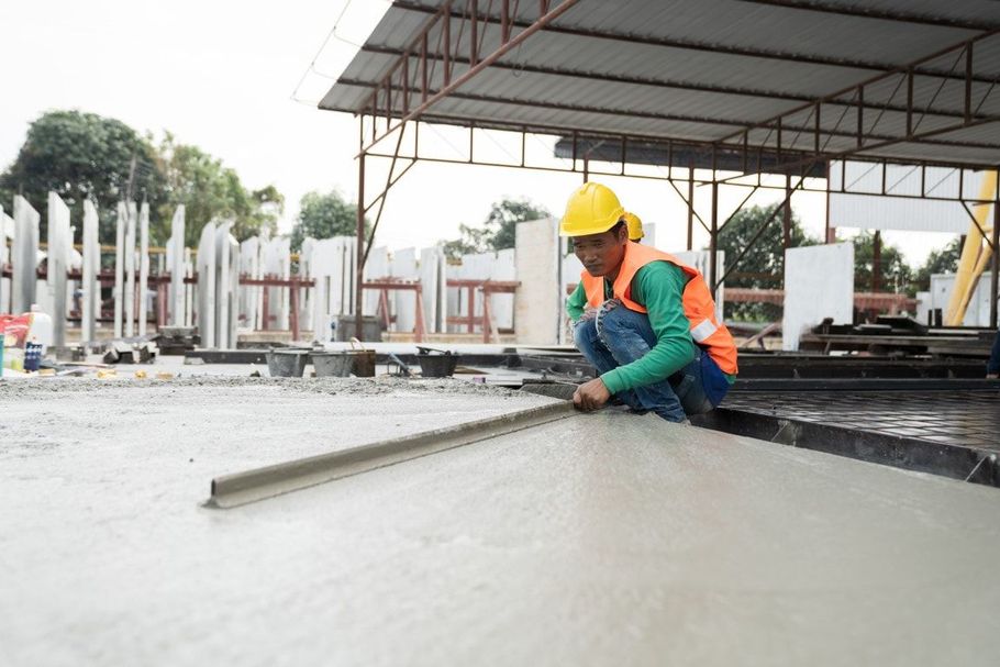 Construction worker smoothing wet concrete on a slab under a roofed structure