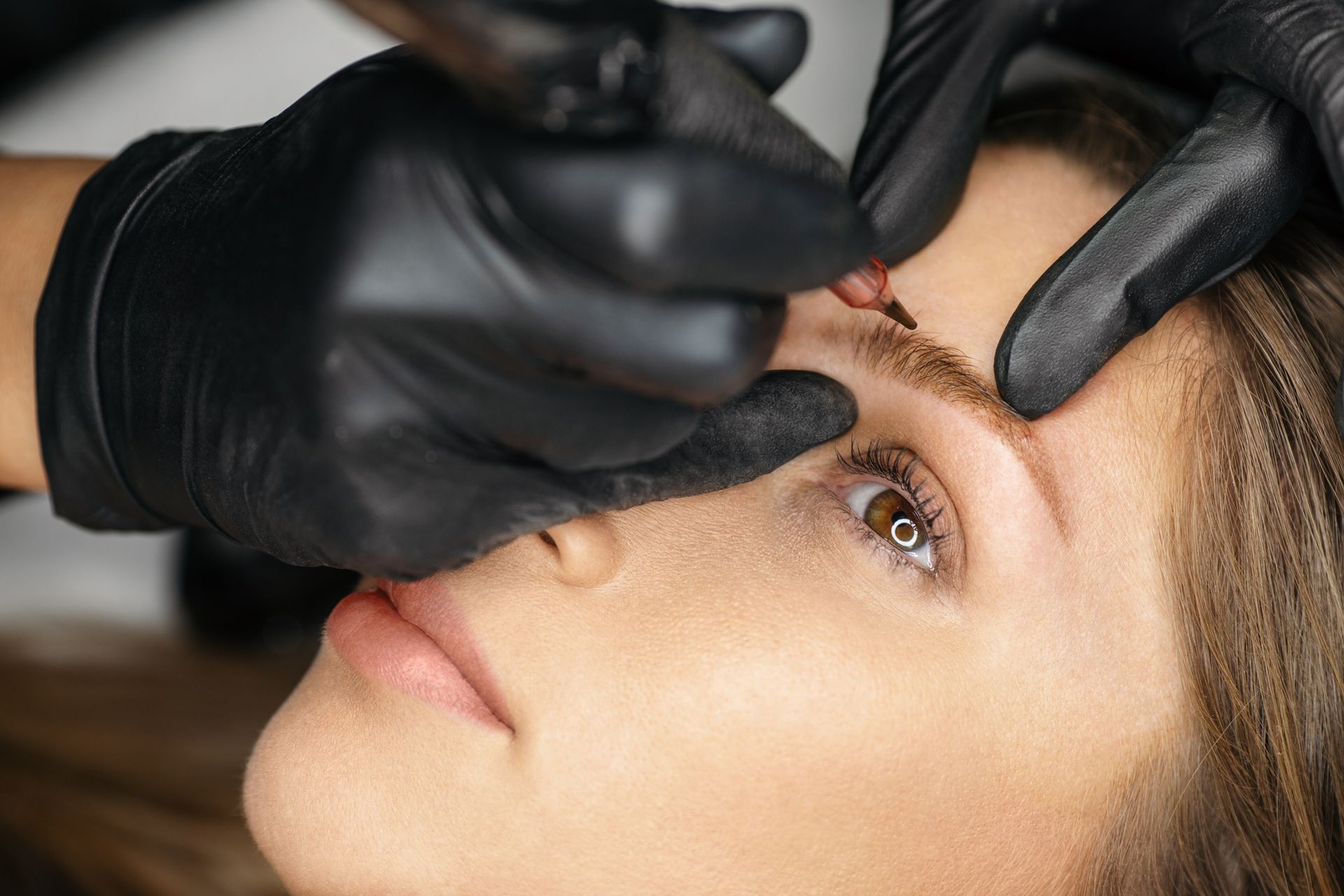 A woman is getting her eyebrows tattooed by a tattoo artist.