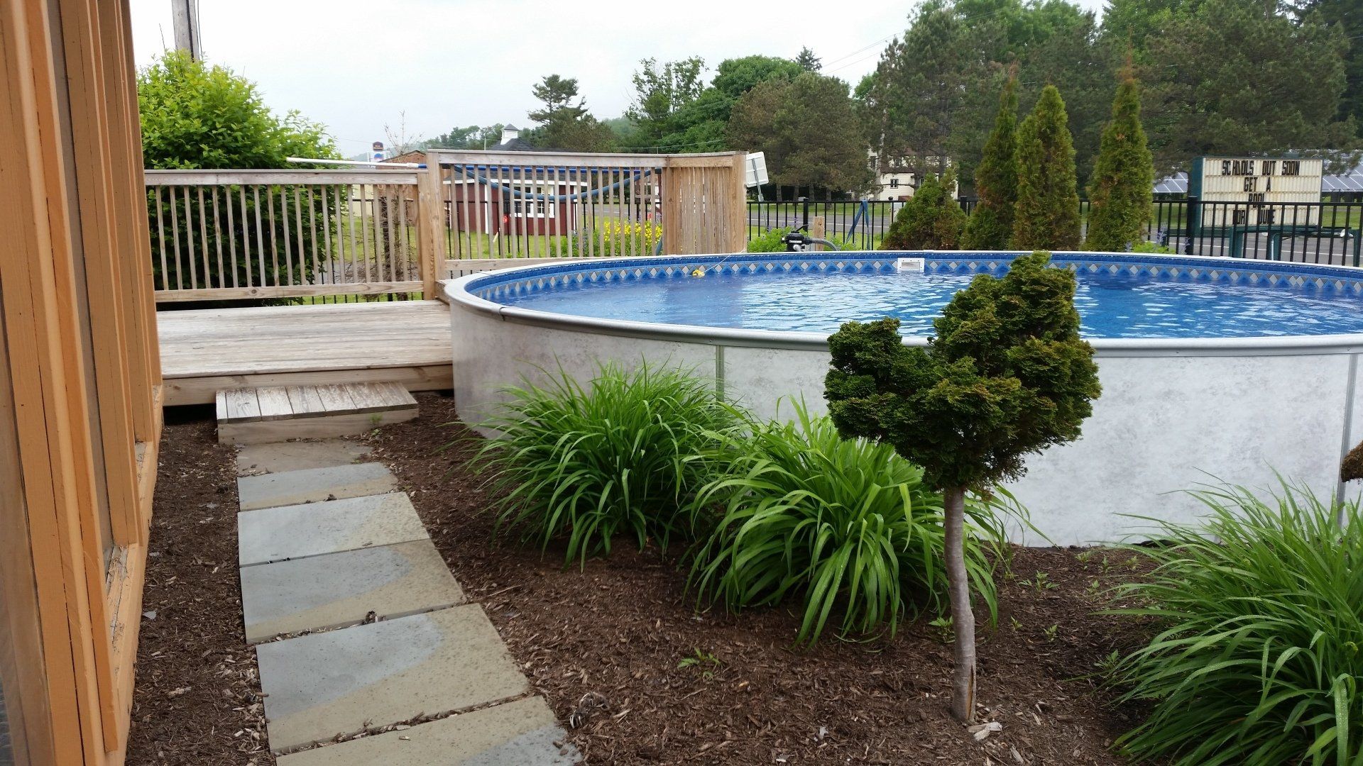 Backyard pool with stone walkway, wooden fence, and landscaped shrubs