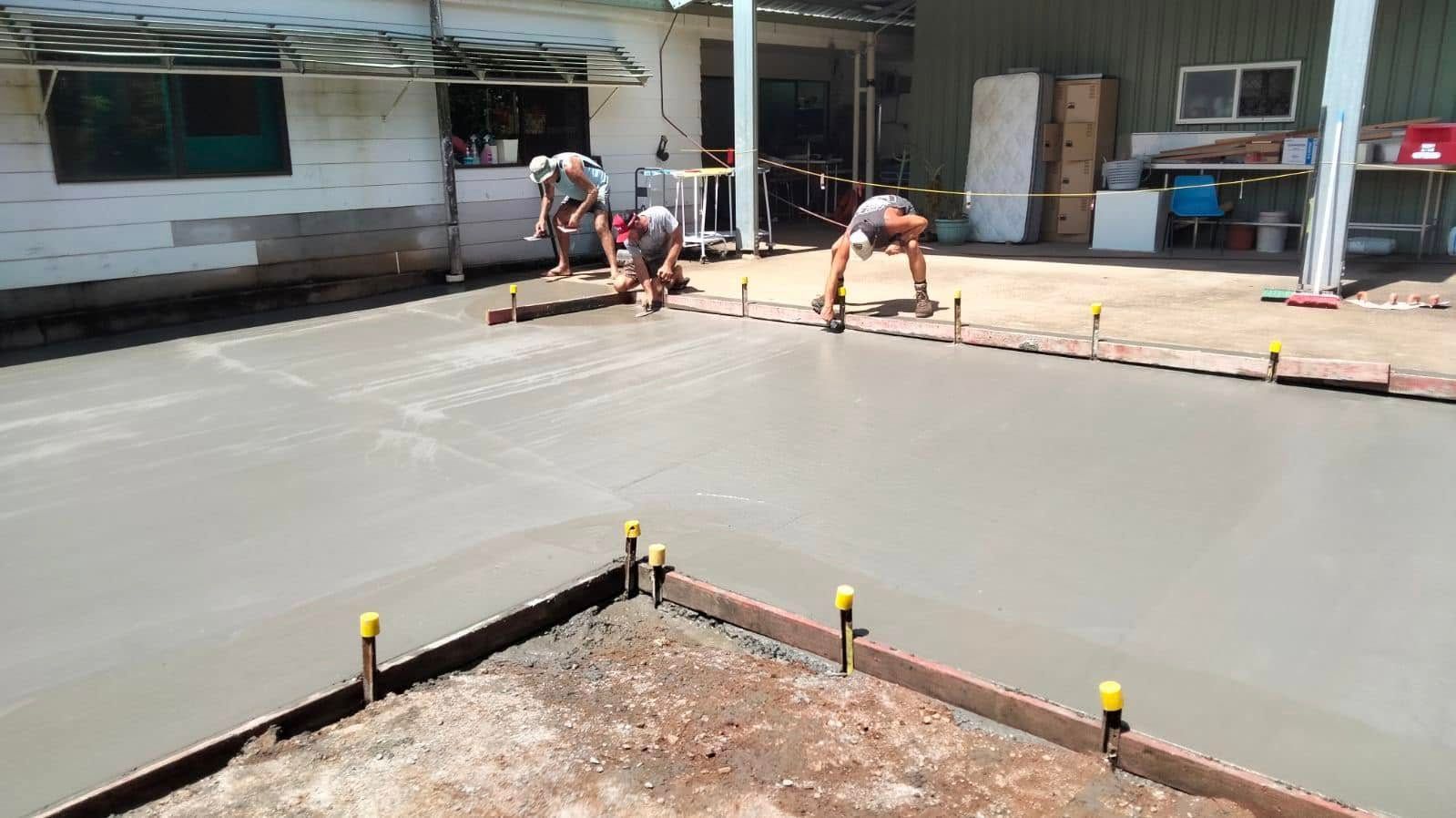 Workers smoothing fresh concrete in an outdoor construction area beside a building. — King Reef Concrete in Kurrimine Beach, QLD