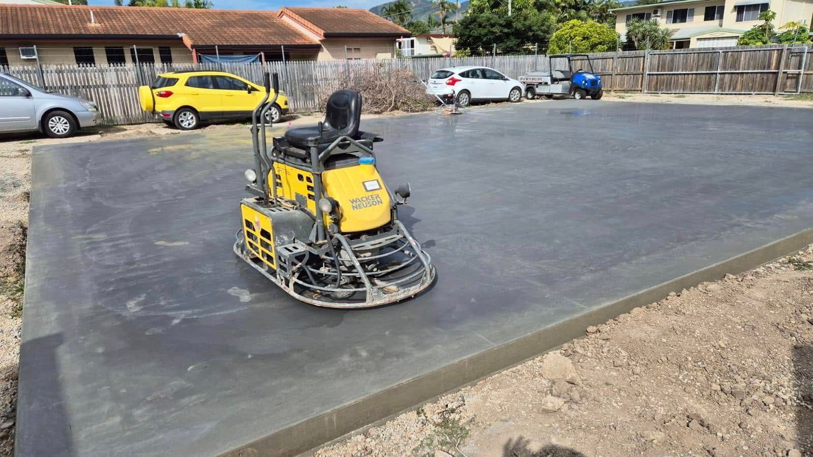Yellow construction machine smoothing fresh concrete on a driveway beside a house — King Reef Concrete in Kurrimine Beach, QLD