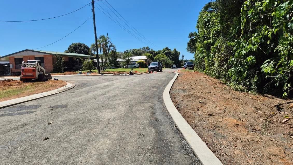 Newly paved road curving past a house and trees on a sunny day — King Reef Concrete in Kurrimine Beach, QLD