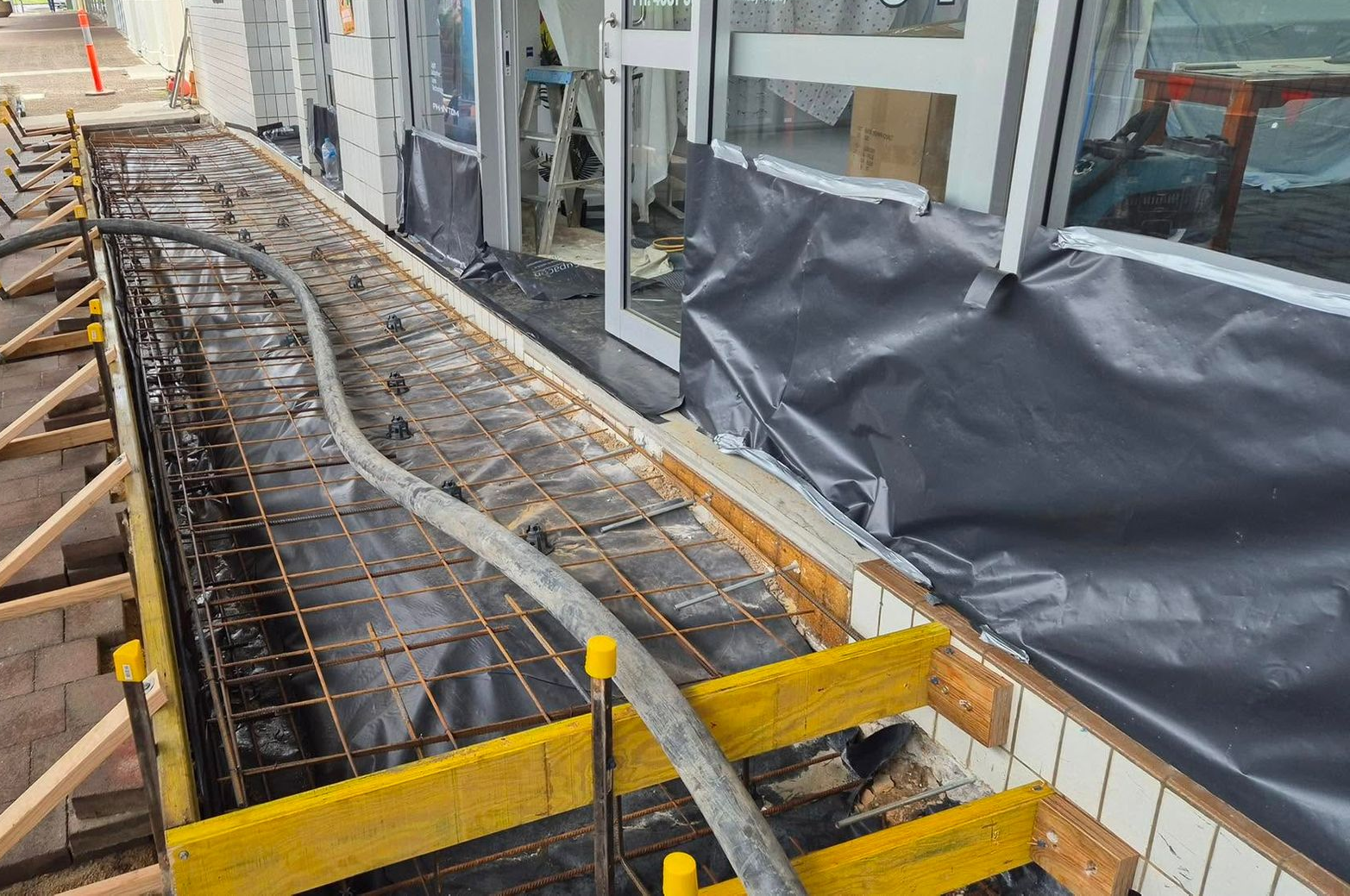 Construction site with rebar foundation forms beside a building walkway and windows