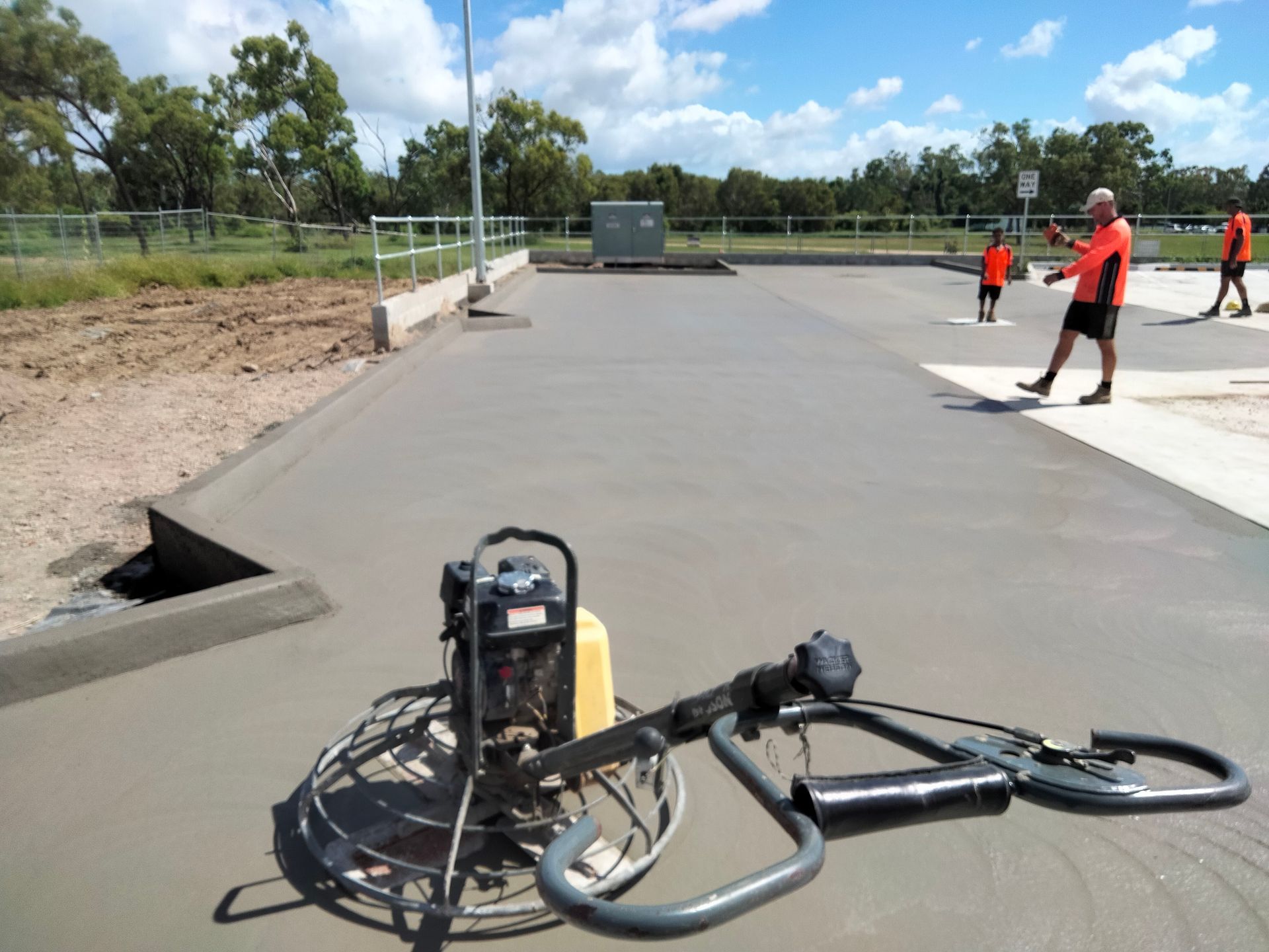 Bicycle and motorcycle on a paved track with workers in orange vests nearby, under a blue sky — King Reef Concrete in Kurrimine Beach, QLD