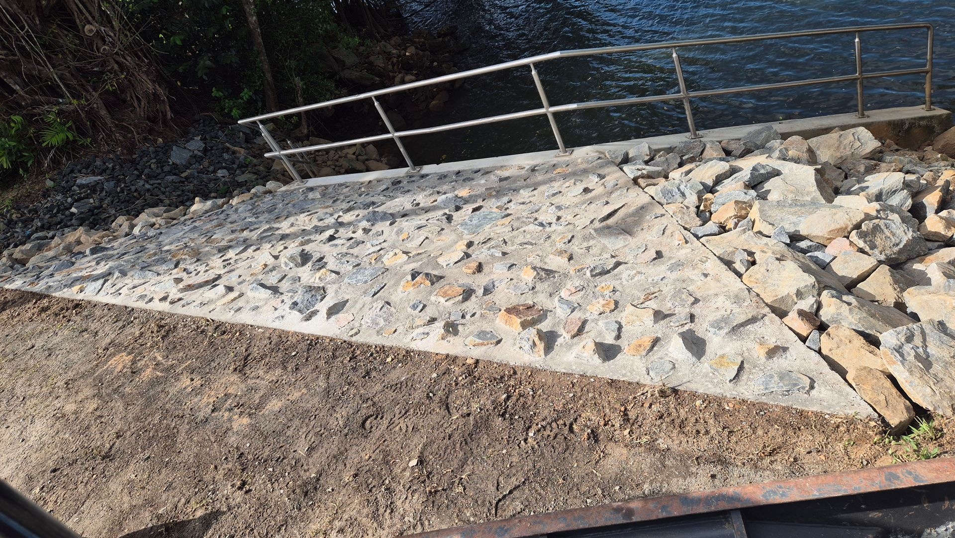 Stone ramp with metal railing beside dirt and water, damaged with scattered rocks and debris — King Reef Concrete in Kurrimine Beach, QLD