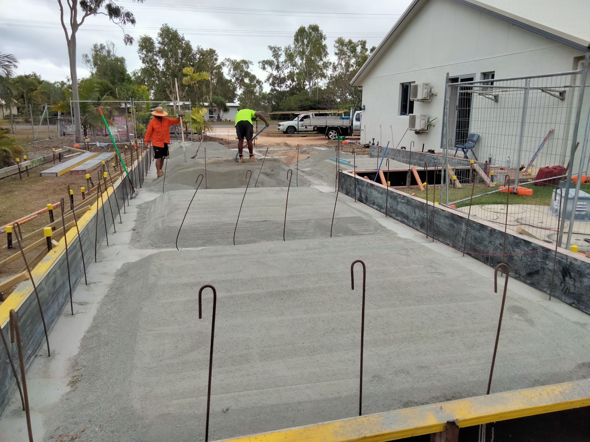 Concrete patio construction with workers, rebar, and fresh poured slabs beside a house — King Reef Concrete in Kurrimine Beach, QLD