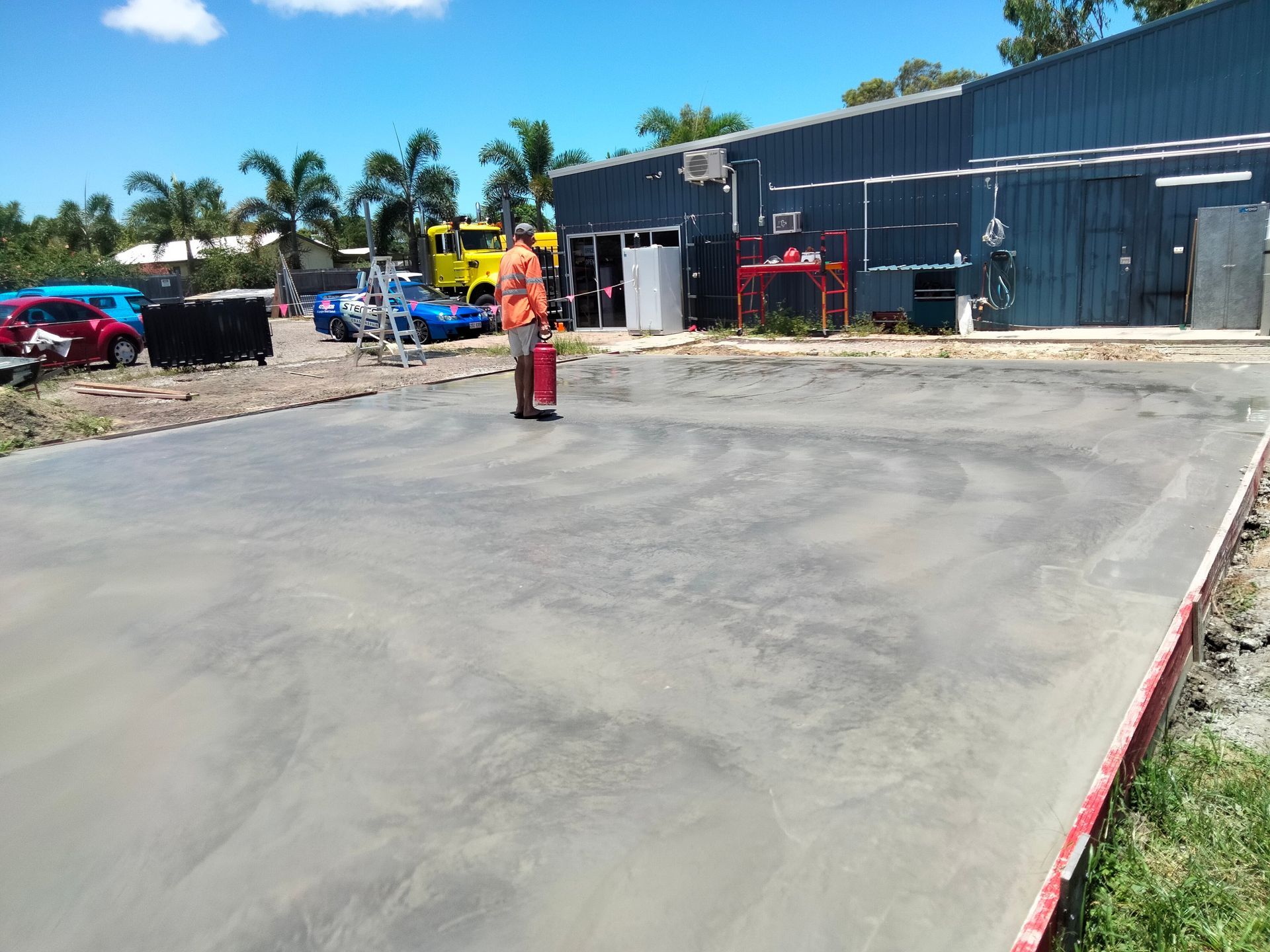 Construction worker on a paved lot beside industrial buildings and equipment under a bright blue sky — King Reef Concrete in Kurrimine Beach, QLD