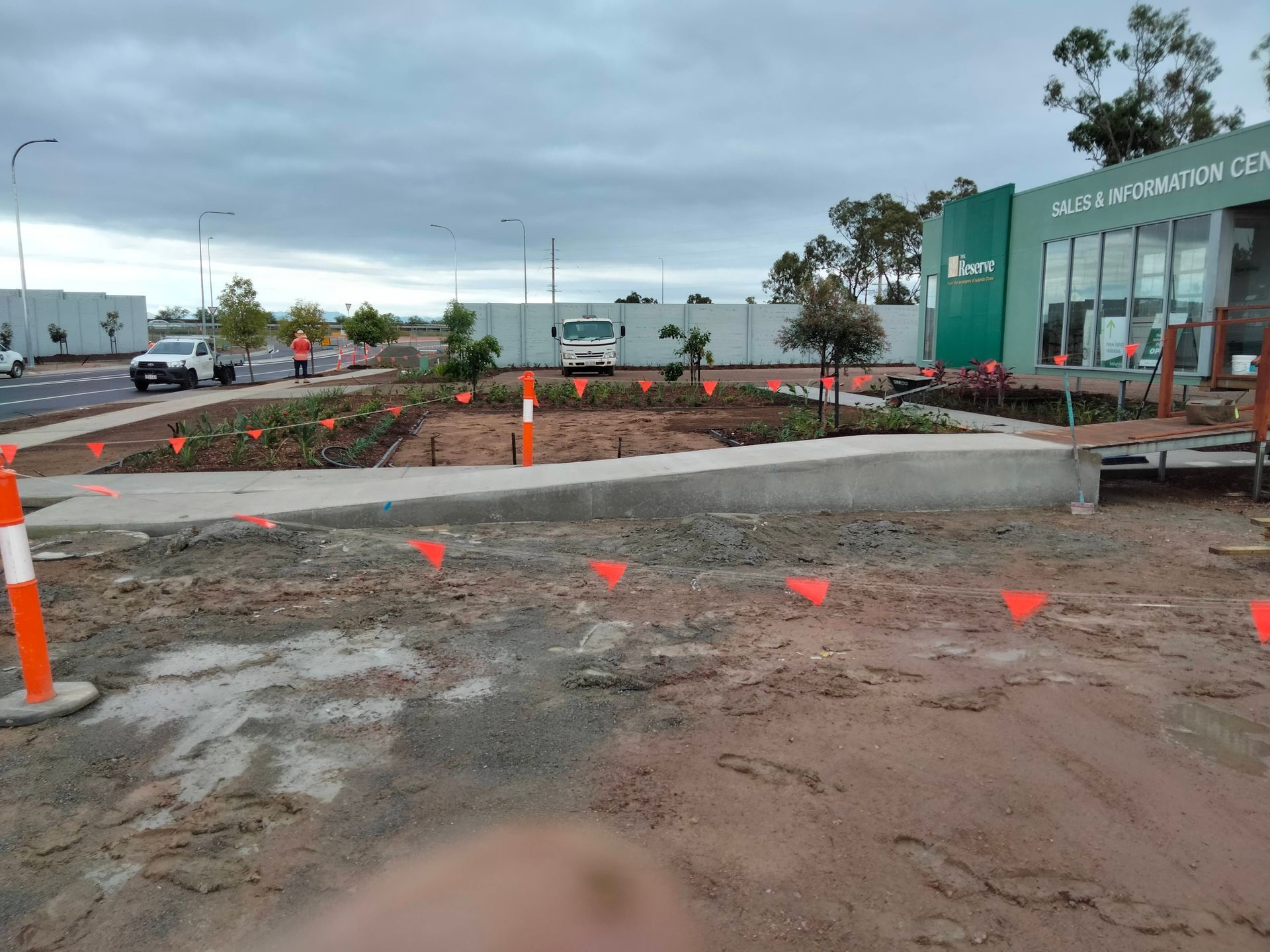 Construction site with orange cones and dirt road beside a green building under cloudy sky — King Reef Concrete in Kurrimine Beach, QLD
