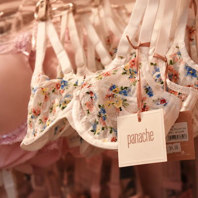 Floral baby onesies on hangers with a pink “panache” tag in a clothing store