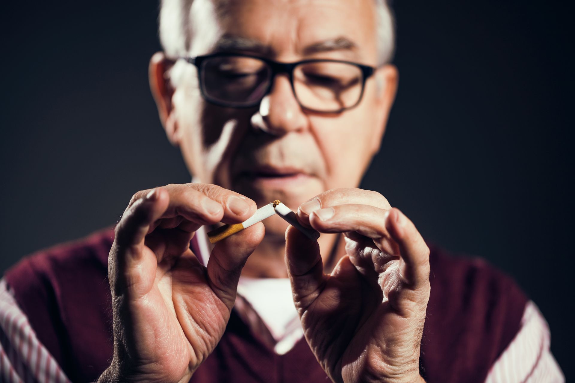 An individual wearing glasses breaks a cigarette in two, symbolizing the decision to quit smoking.