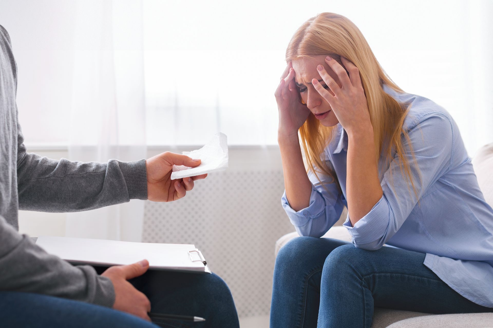 A person sitting with their head in their hands while a counselor offers them a tissue during a therapy session.
