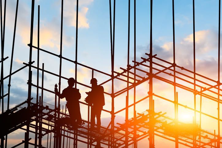 Due operai edili sono in piedi su un'impalcatura in un cantiere al tramonto.
