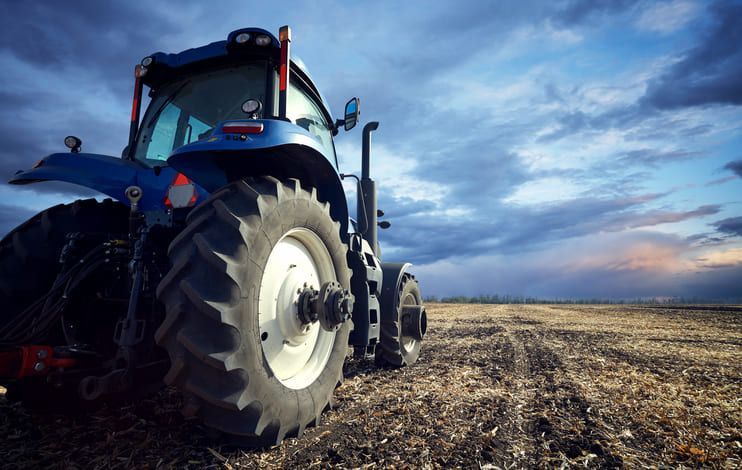 Un trattore blu è parcheggiato in un campo con un cielo nuvoloso sullo sfondo.