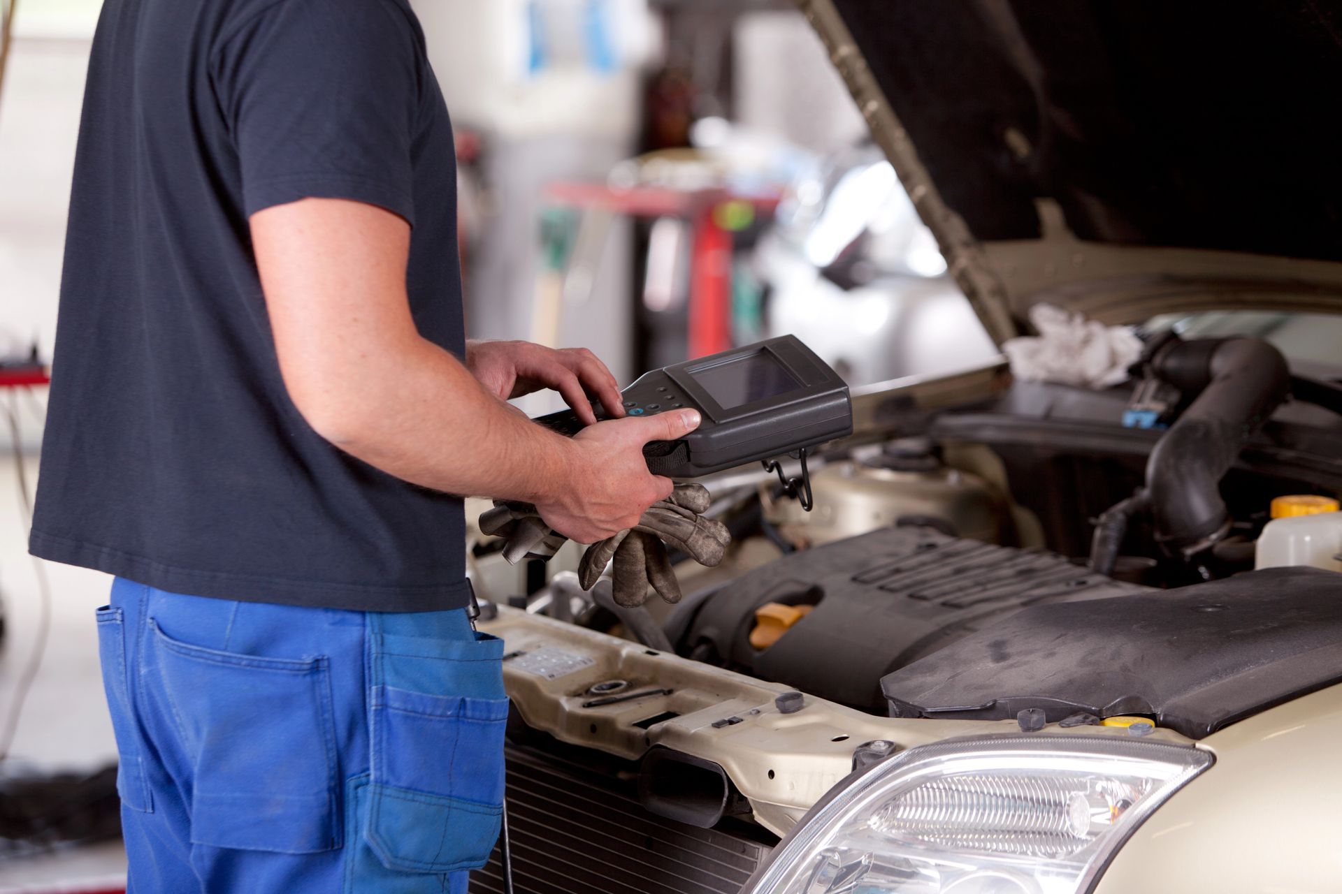 Mecánico utilizando un escáner de diagnóstico bajo el capó de un coche en un taller de reparación.