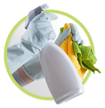 Gloved hand spraying cleaner onto a white bottle with colorful cleaning cloths