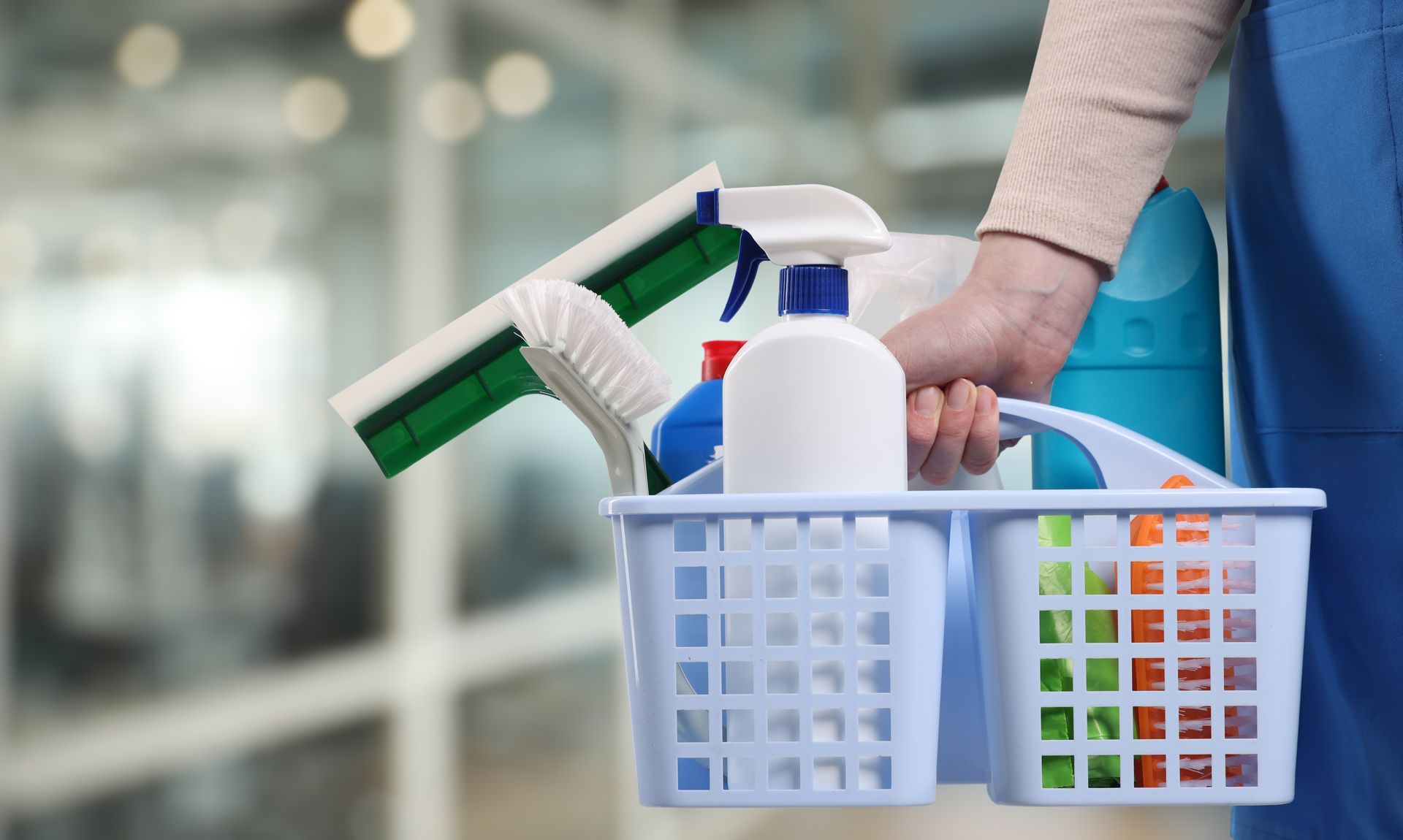 Person carrying a caddy of cleaning supplies, including sprays and bottles, in a store aisle