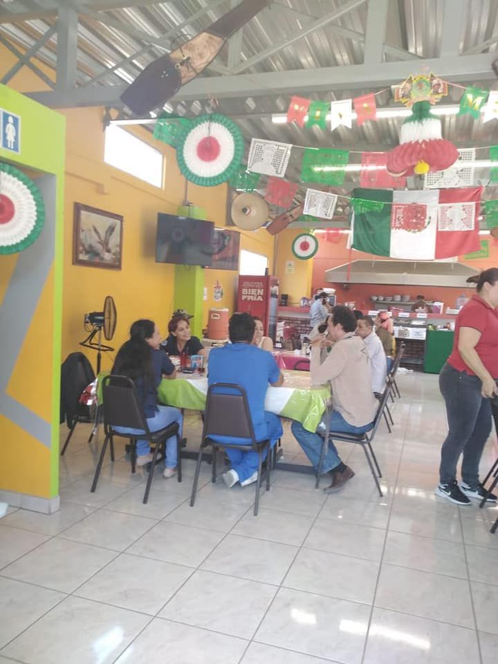 People sit at tables inside a restaurant decorated with Mexican flag-themed garlands and paper cutouts.