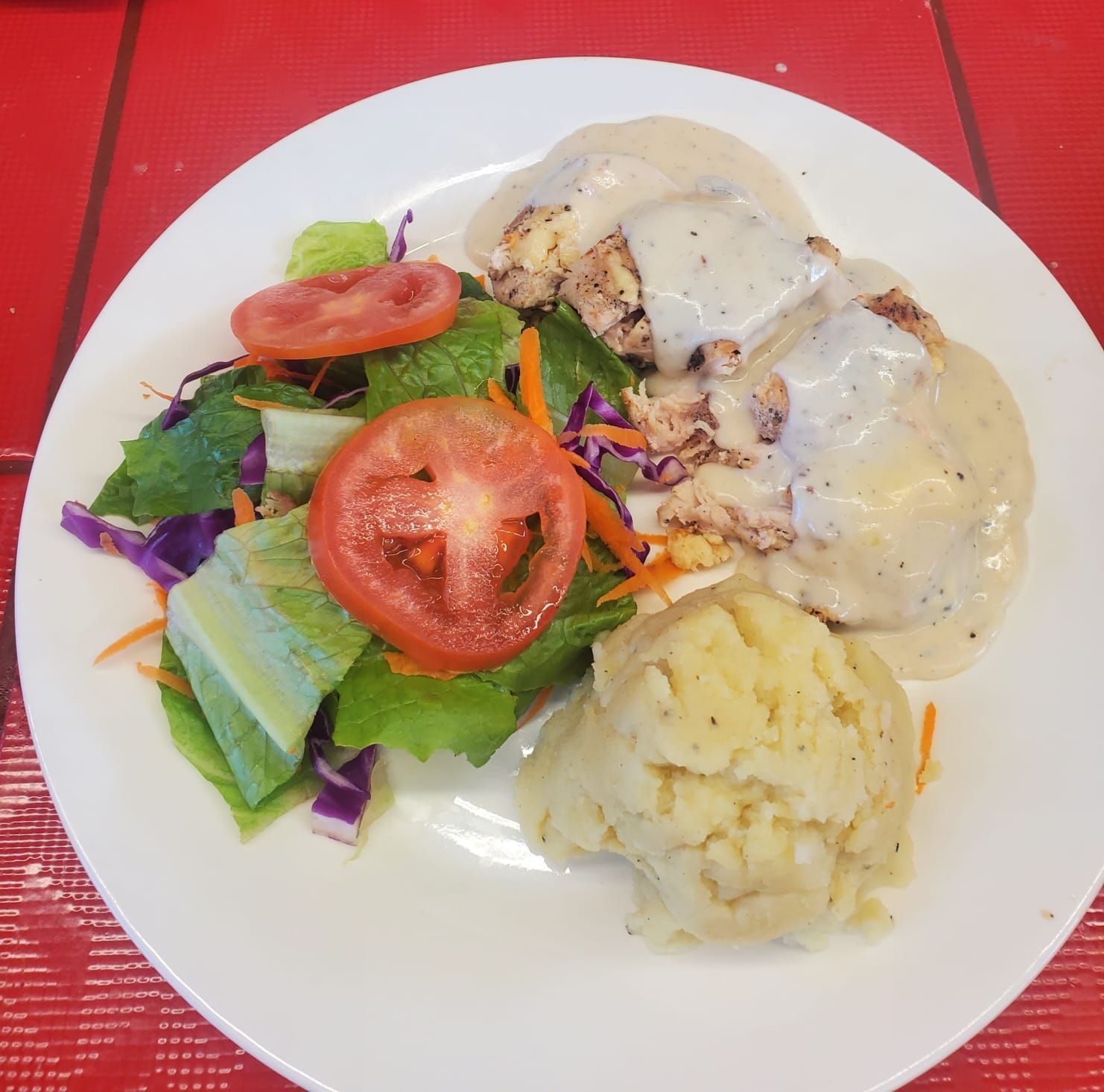 A plate with a side salad of greens and tomatoes, a serving of mashed potatoes, and sliced meat topped with gravy.