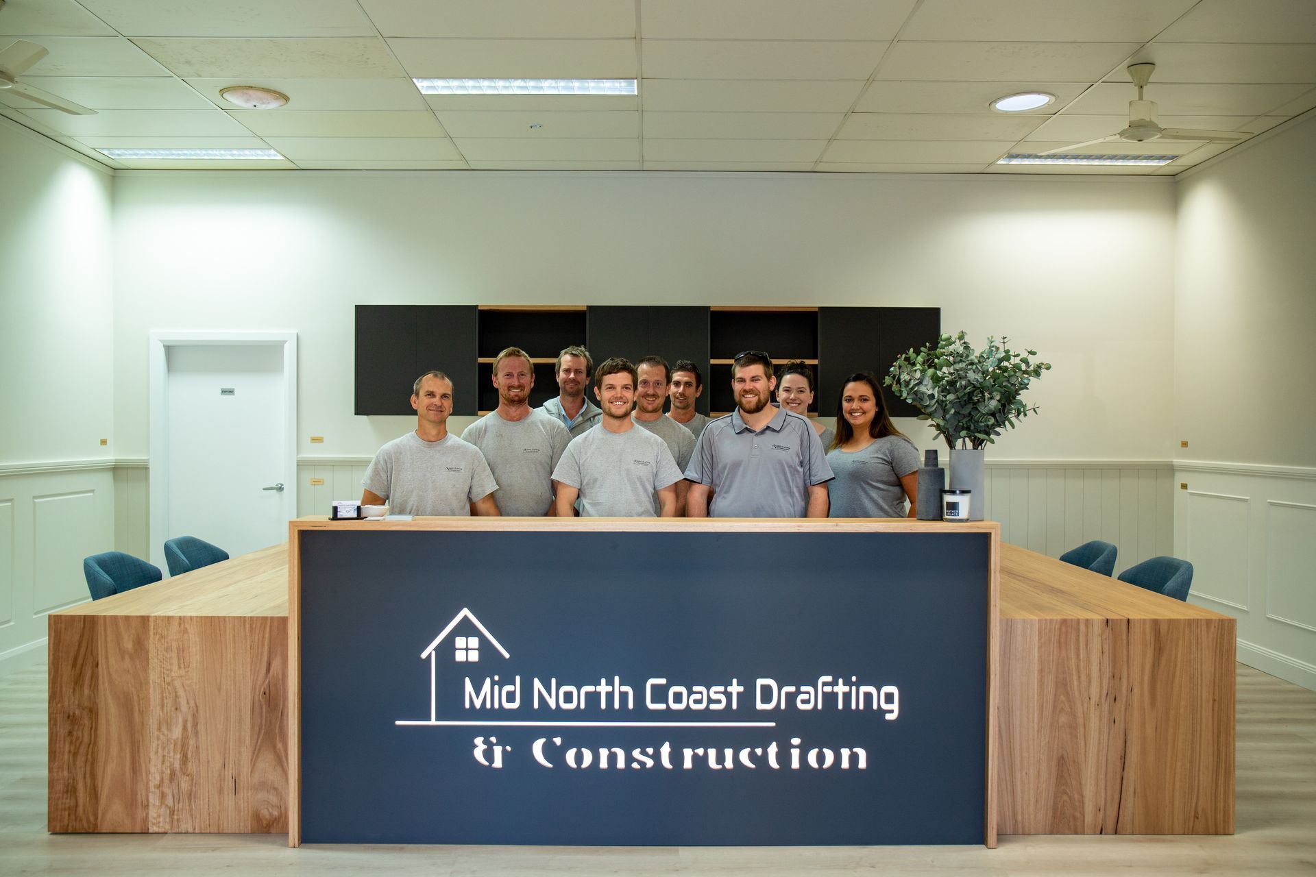 Mid North Coast Drafting & Construction team standing behind a reception desk with the company logo in Taree, NSW.