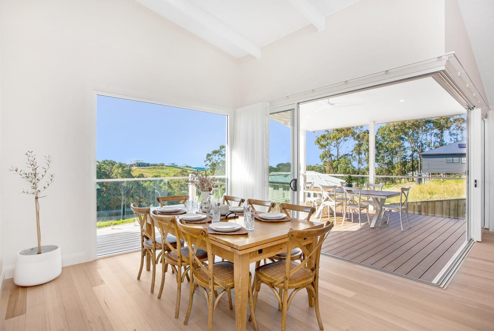 A dining room with a wooden table and deck access, showcasing a home designed by a Builder Taree service in Taree, NSW.