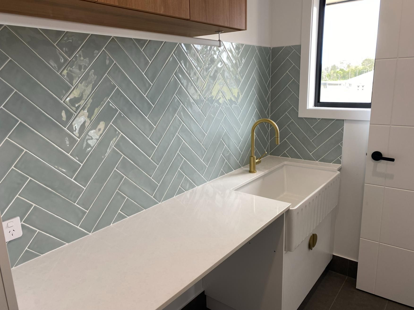 Laundry Room With Blue Herringbone Tile, White Sink, and Gold Faucet — Mid North Coast Drafting & Construction in Taree, NSW
