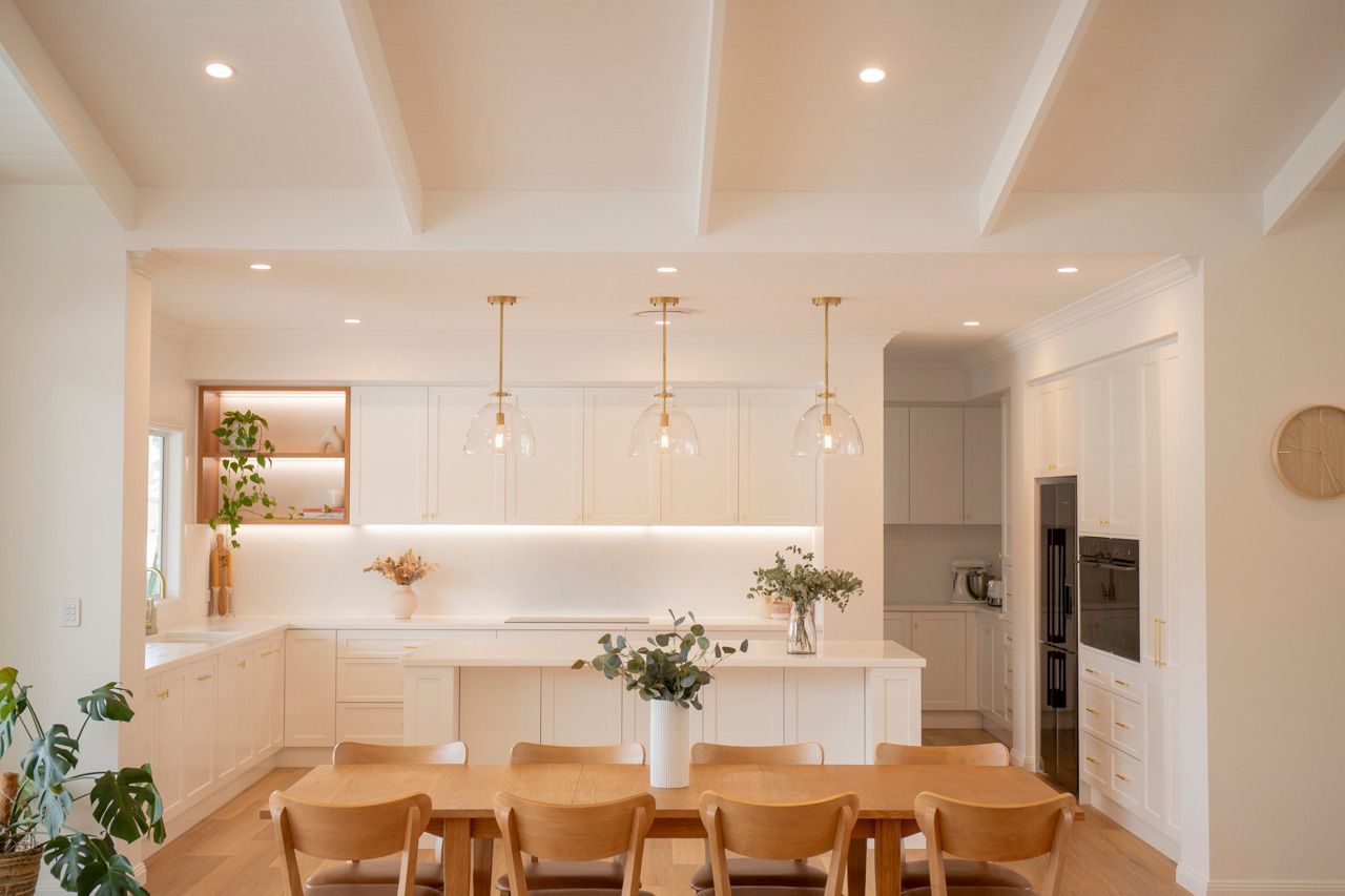 Modern Kitchen With White Cabinets, Wooden Table, and Pendant Lights — Mid North Coast Drafting & Construction in Taree, NSW