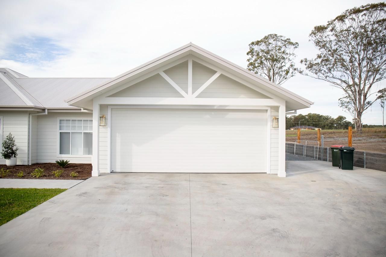 White House With Concrete Driveway and Closed Garage Door — Mid North Coast Drafting & Construction in Taree, NSW