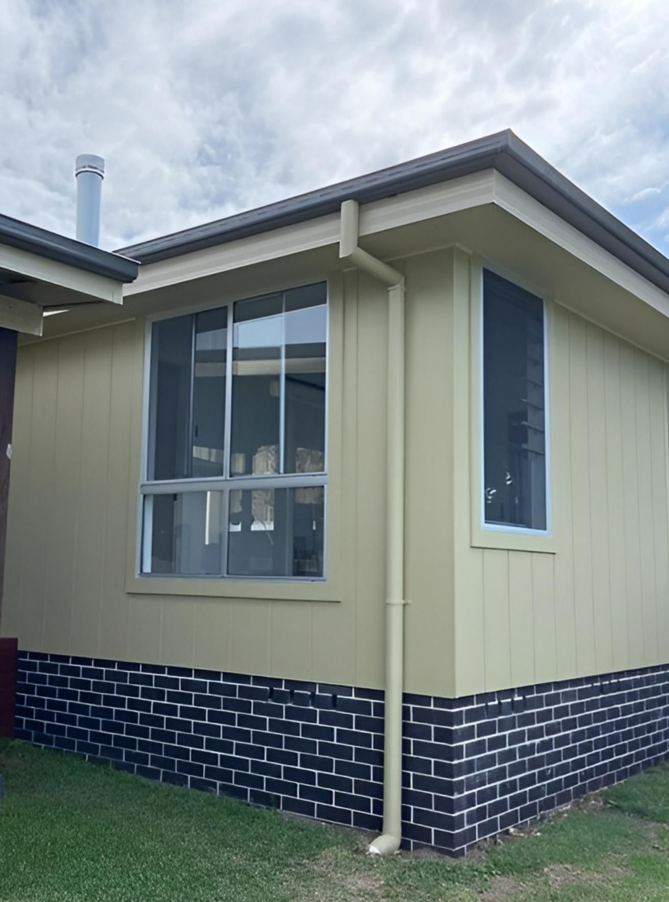 A Light Tan House With a Black Brick Base and Two Windows — Mid North Coast Drafting & Construction in Nabiac, NSW