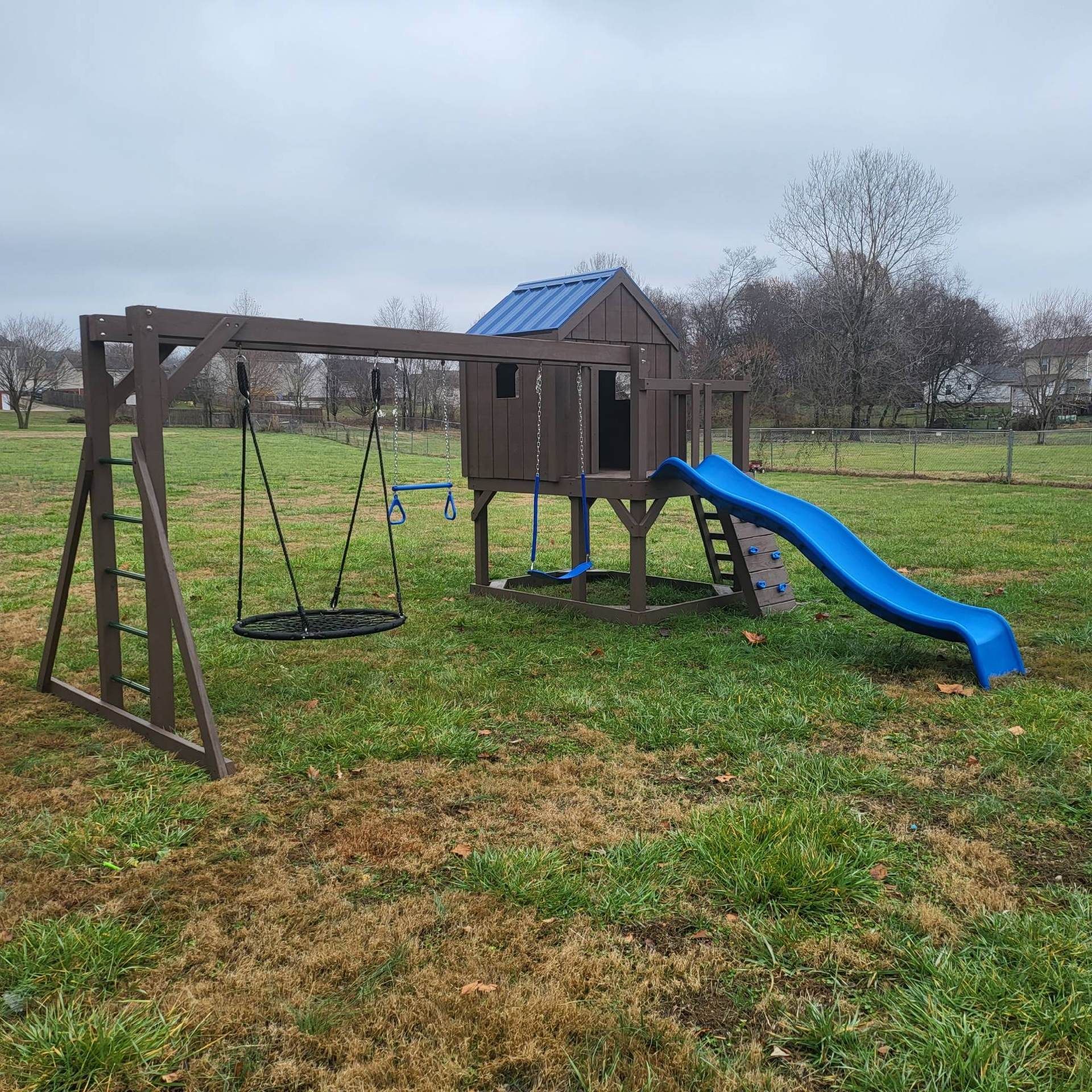 Wooden playset with swings, a slide, and a small playhouse on a cloudy day.