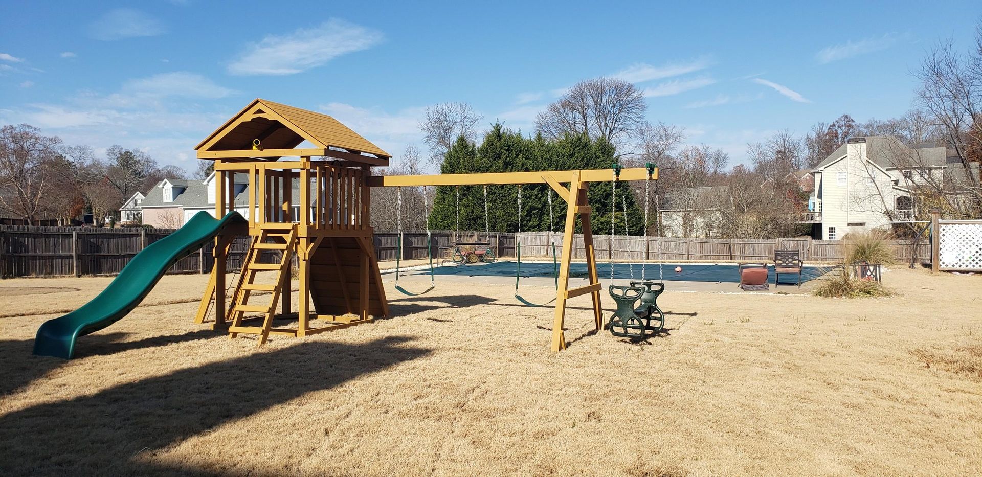 Playground with slide, swings, and playhouse in a backyard on a sunny day.
