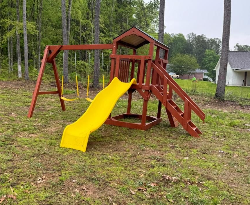 Wooden playset with swings, slide, and climbing stairs in a yard.