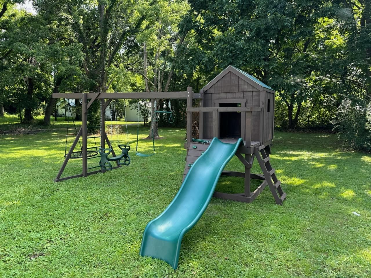 Playground set in a grassy yard with a swing set, playhouse, and slide.
