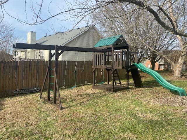 Wooden swing set and playhouse with green slide in a backyard.