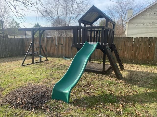 Playground set with swing set, slide, and fort in a grassy backyard.