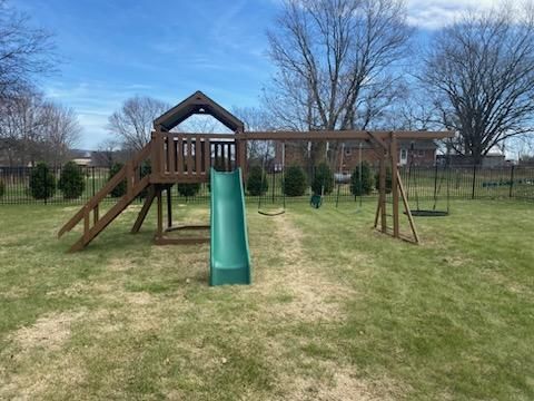 Wooden playset in a grassy backyard, with a slide, swings, and climbing structure.
