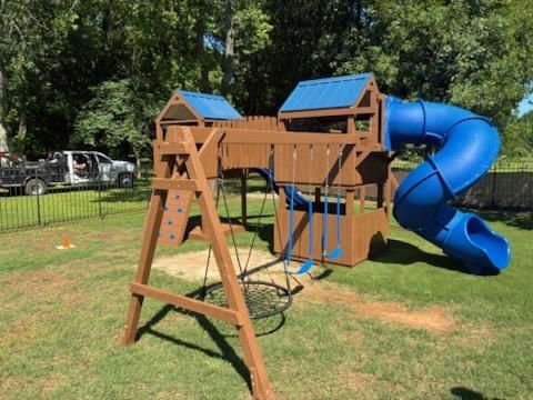 Wooden backyard playset with blue roof panels and a blue spiral slide on grass.