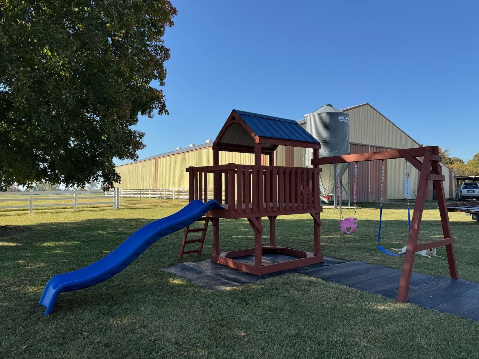 Playground with blue slide, swing set, and a large building in the background on a sunny day.