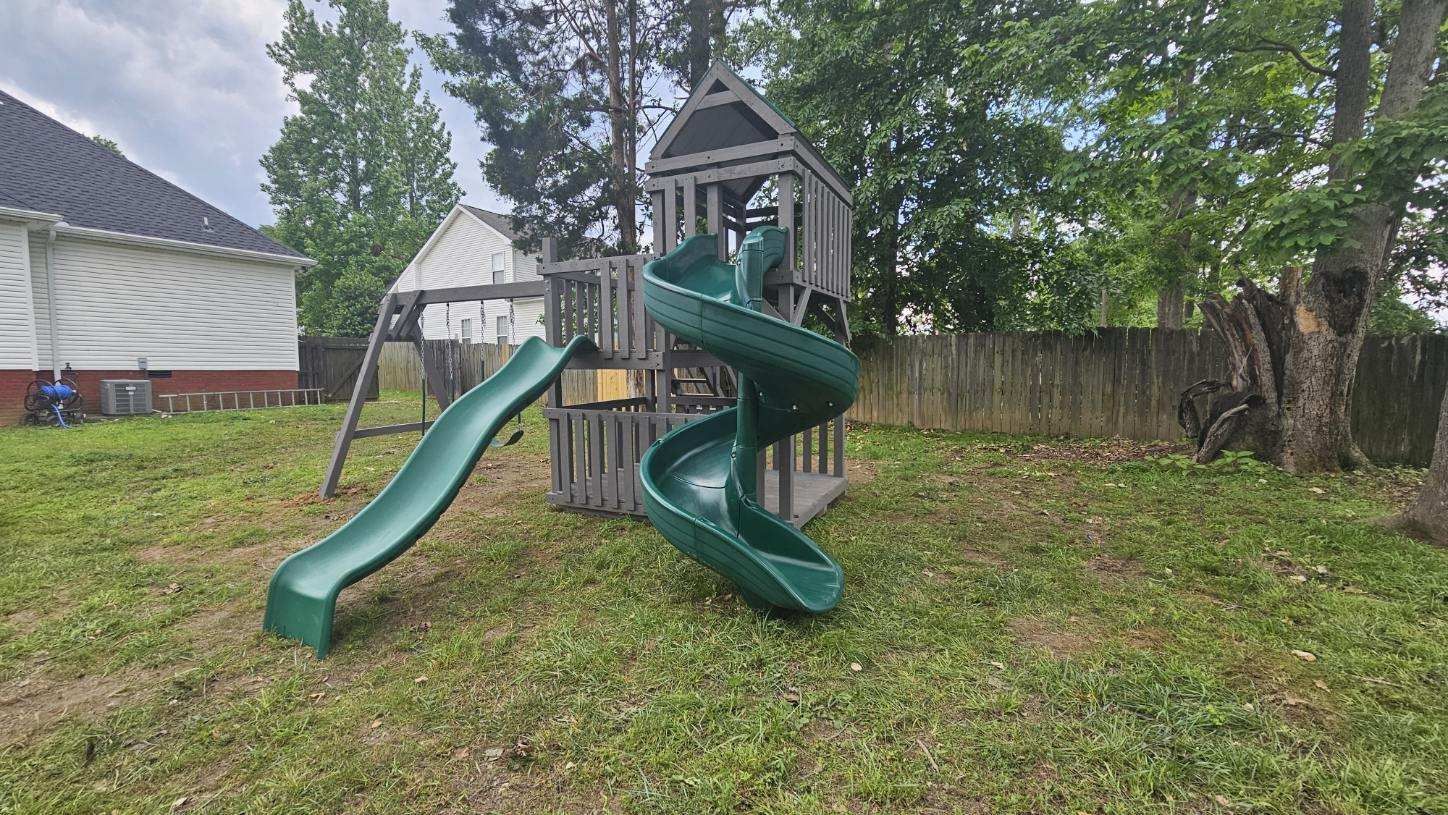 A wooden playset with green slides in a grassy backyard.