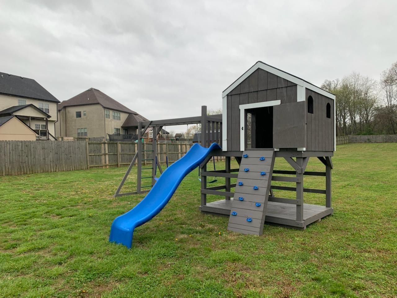 Children's backyard play set with blue slide and climbing wall on a grassy lawn
