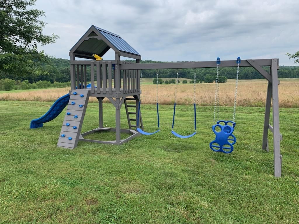 Blue slide on a wooden playground set in a grassy park under a partly cloudy sky.